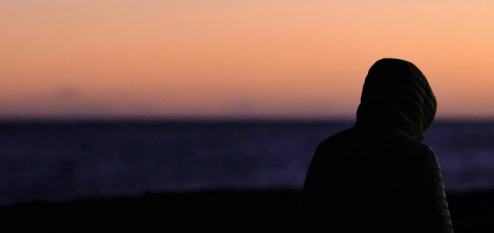person wearing hoodie walking near shore