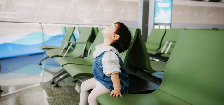 A young child sits on a green bench looking up.